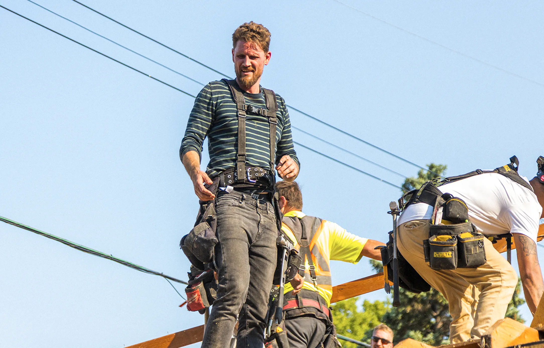 David on a job site, harnessed in on a roof frame with the crew